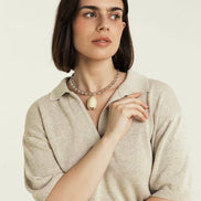 Woman wearing a beige sweater and necklace against a plain background