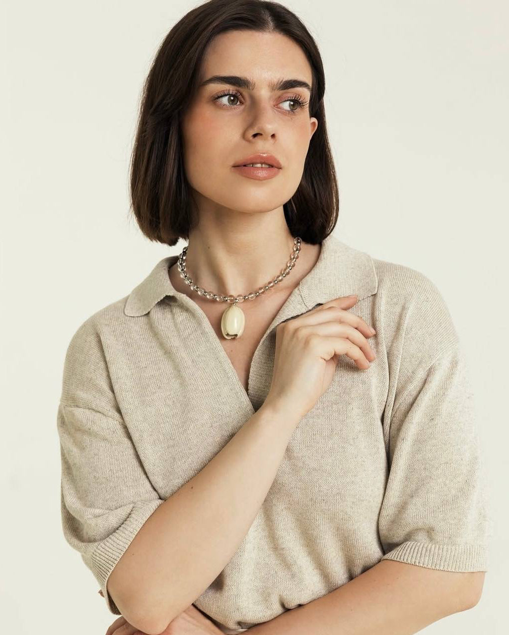 Woman wearing a beige sweater and necklace against a plain background