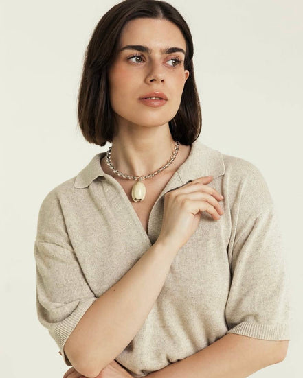 Woman wearing a beige sweater and necklace against a plain background