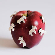 Red apple with silver horse-shaped charms on a light gray background