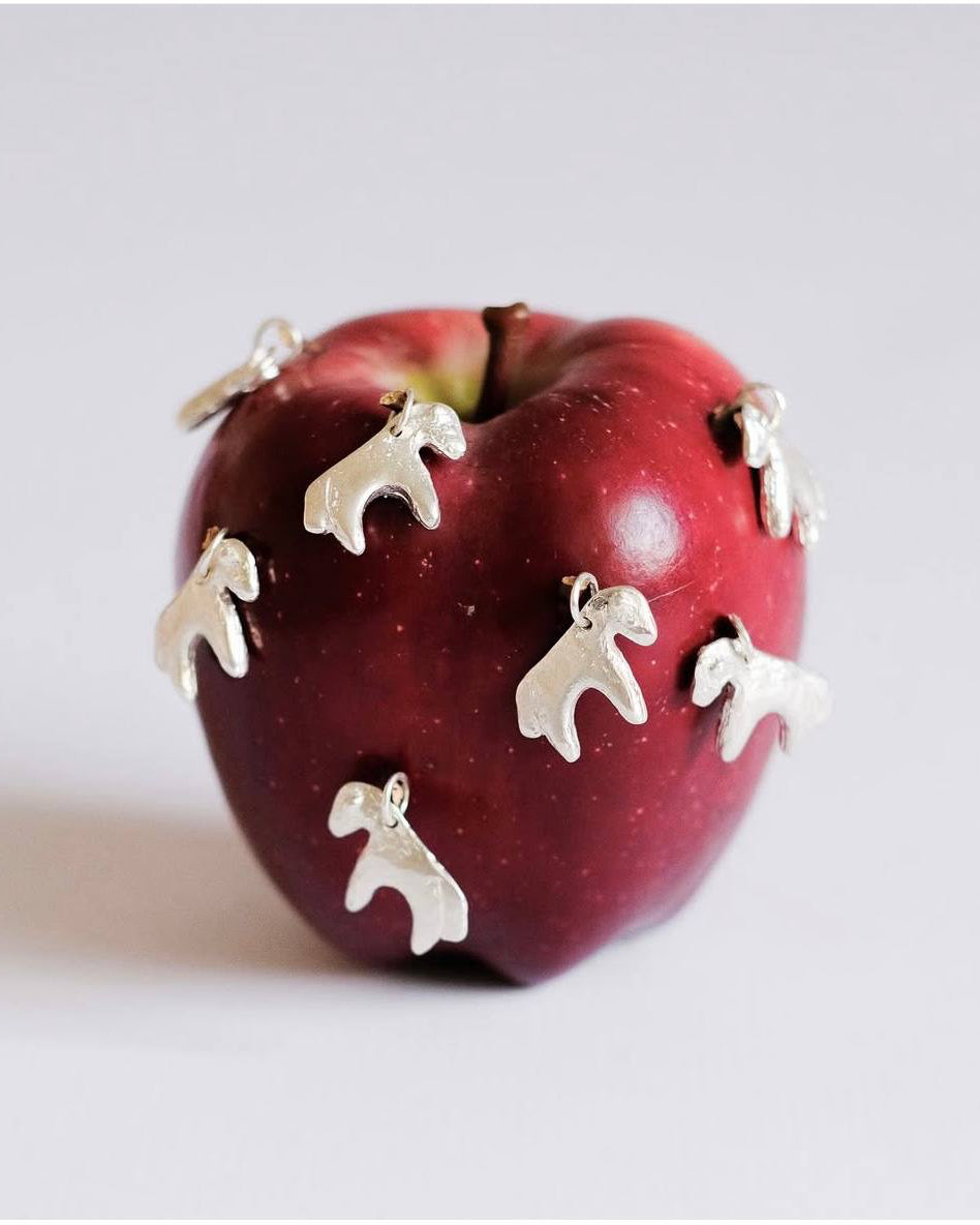 Red apple with silver horse-shaped charms on a light gray background