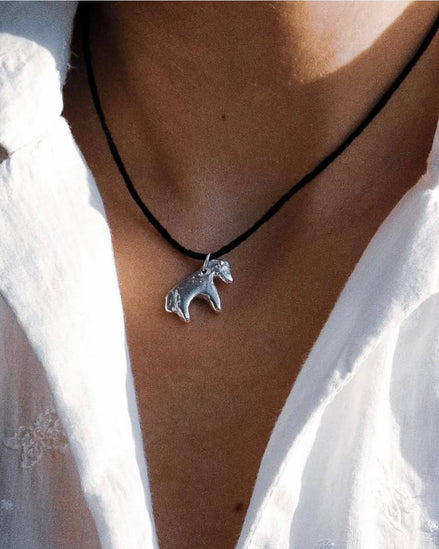 Necklace with a horse pendant worn by a person in a white shirt.