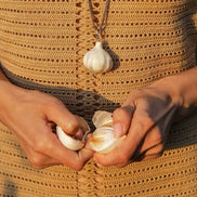 Person holding garlic bulbs with a necklace featuring a garlic pendant.