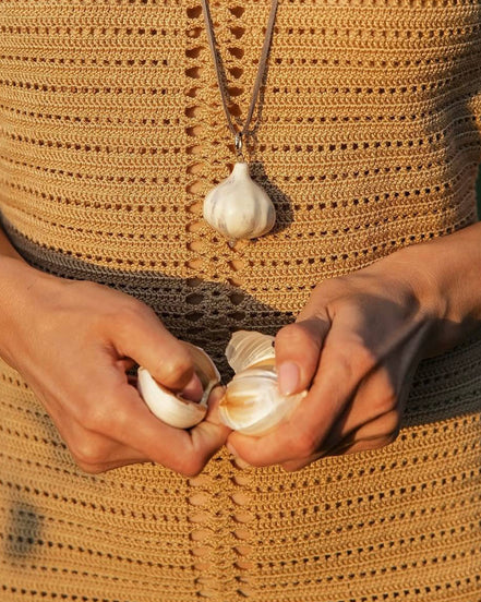 Person holding garlic bulbs with a necklace featuring a garlic pendant.