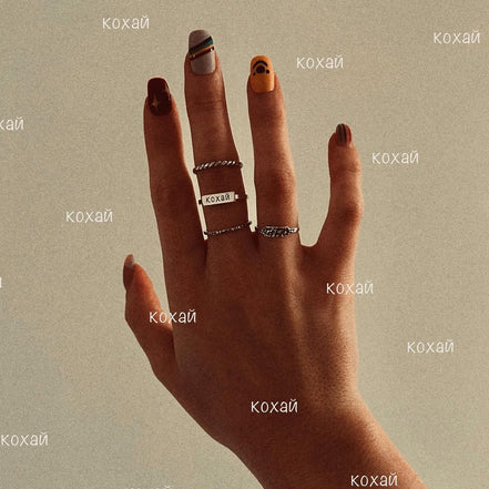 Hand wearing multiple silver rings with engraved text.