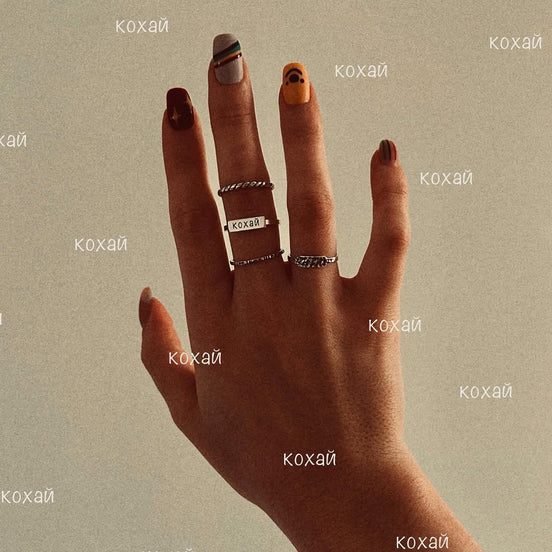 Hand wearing multiple silver rings with engraved text.