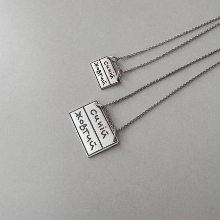 Silver necklace with engraved text.